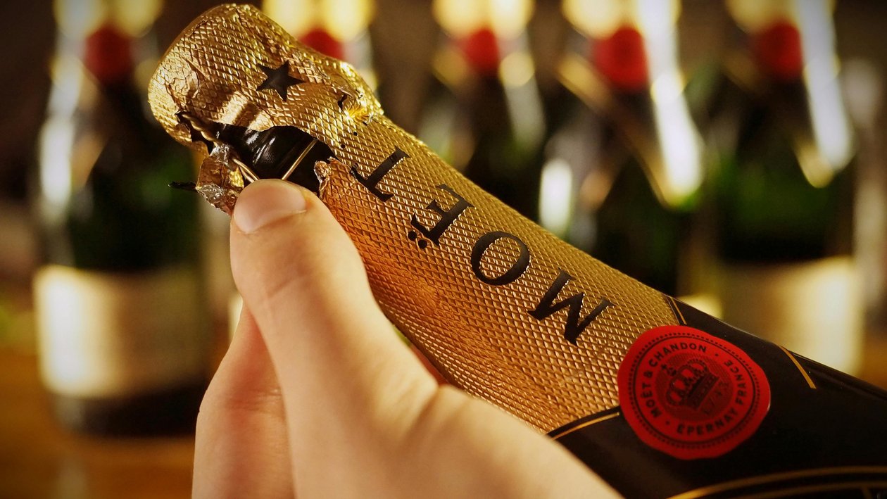 Champagnerfreude erleben Eine Person öffnet eine Flasche Moët Champagner, im Hintergrund weitere unscharfe Flaschen.