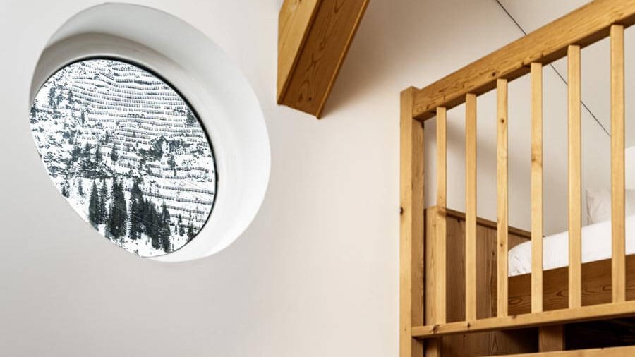 Moderne Juniorsuite mit Bergblick Helle, moderne Juniorsuite mit rundem Fenster und Blick auf verschneite Berge, Holzdetails im Raum.