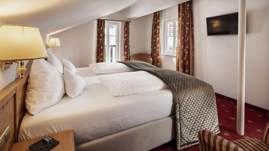 Moderne Familiensuite im Tannberger Hof Familienzimmer mit Doppelbett und gemütlicher Sitzecke in modernem Design. Weißes Bettzeug und dekorativer Überwurf sind zu看到