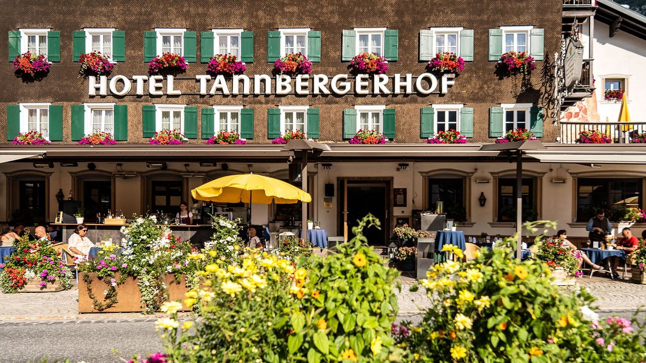 Alpine Lodge im Sommer Außenansicht des Hotels Tannbergerhof mit blühenden Blumen und Terrassenmöbeln vor dem Gebäude