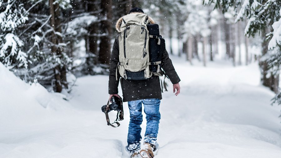 Winterwandern am Arlberg Person wandert durch einen schneebedeckten Wald mit Rucksack und Kamera in der Hand.