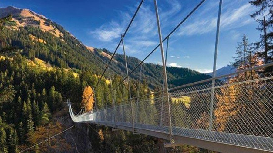 Hängebrücke inmitten der Berglandschaft Suspension bridge crossing a valley surrounded by mountains and forests under a blue sky