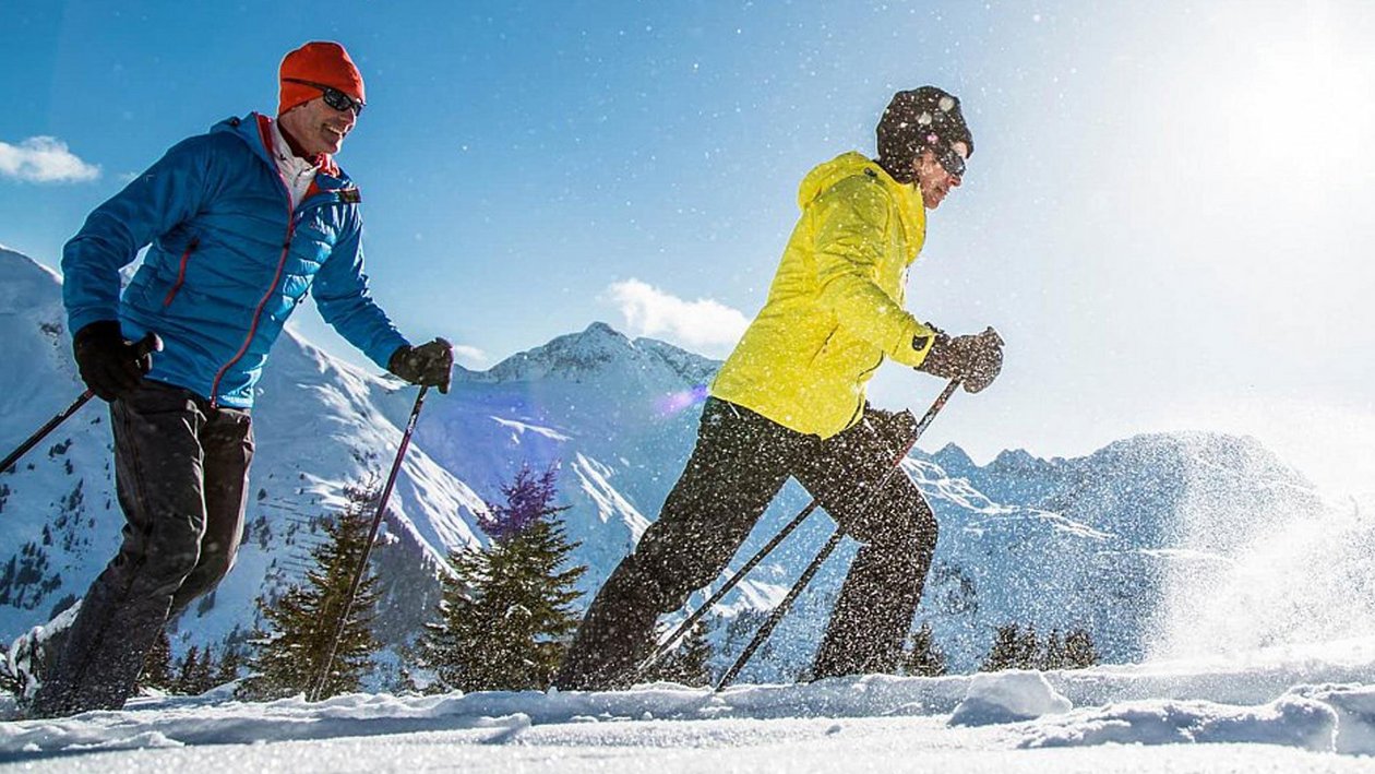 Skifahren im Arlberg Zwei Skifahrer auf einer verschneiten Berglandschaft unter blauem Himmel in den Alpen.
