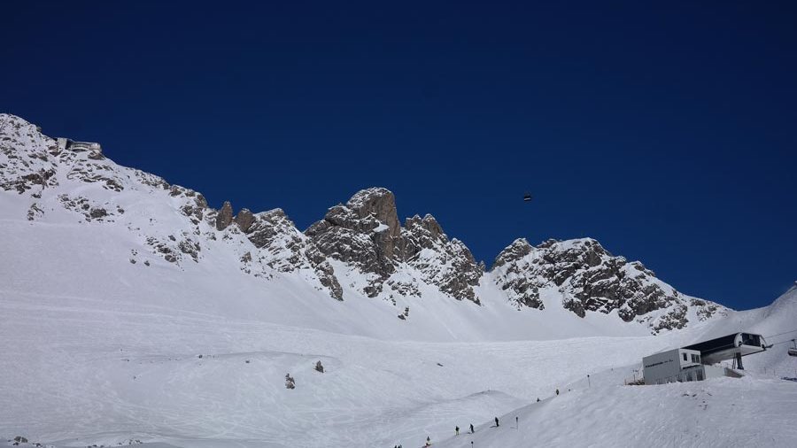 Alpenlandschaft im Winter Schneebedeckte Berge mit Skihängen und einer kleinen Hütte im Vordergrund unter klarem Himmel