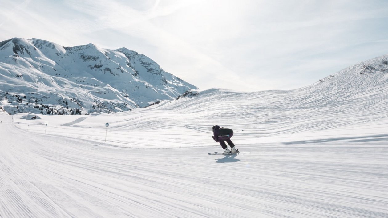 Schneeabenteuer in den Bergen Skifahrer fährt eine schneebedeckte Piste mit Bergen im Hintergrund unter klarem Himmel hinunter