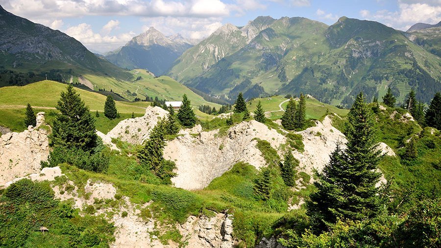 Alpine Landschaft entdecken Alpine Landschaft in Lech am Arlberg mit grünen Wiesen, Felsen und Bergpanorama im Hintergrund