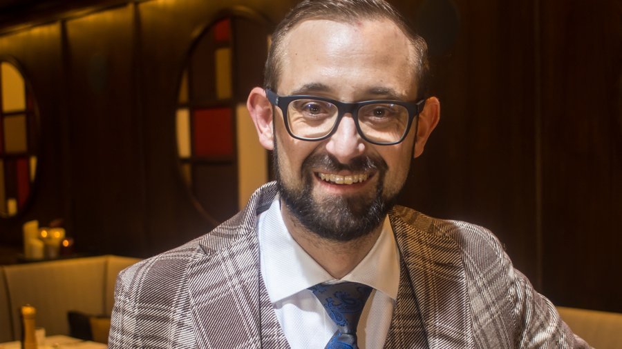Gastgeber Johannes Pfefferkorn Lächelnder Mann in kariertem Anzug und blauer Krawatte im Restaurant mit warmem Licht