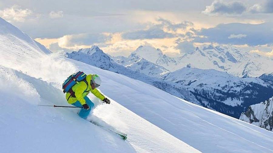 Skiabenteuer in den Bergen Skifahrer fährt eine verschneite Piste mit Berglandschaft im Hintergrund und bewölktem Himmel hinunter