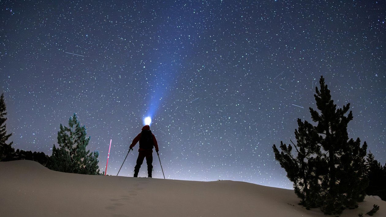 Sternenhimmel in den Bergen Silhouette einer Person mit Stirnlampe auf schneebedecktem Gelände unter einem sternenübersäten Himmel