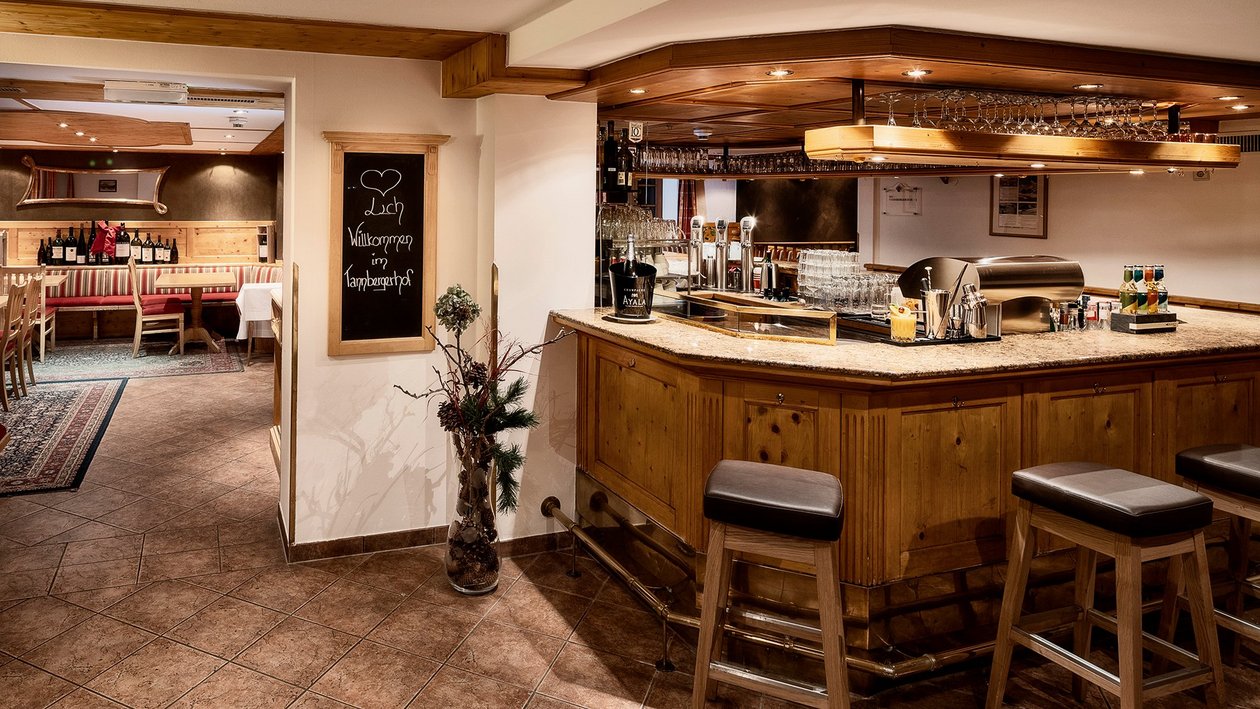 Gemütliche Bar mit Holzinterieur Barbereich mit Holzmöbeln und Tresen, angrenzender Speisebereich im Restaurant sichtbar