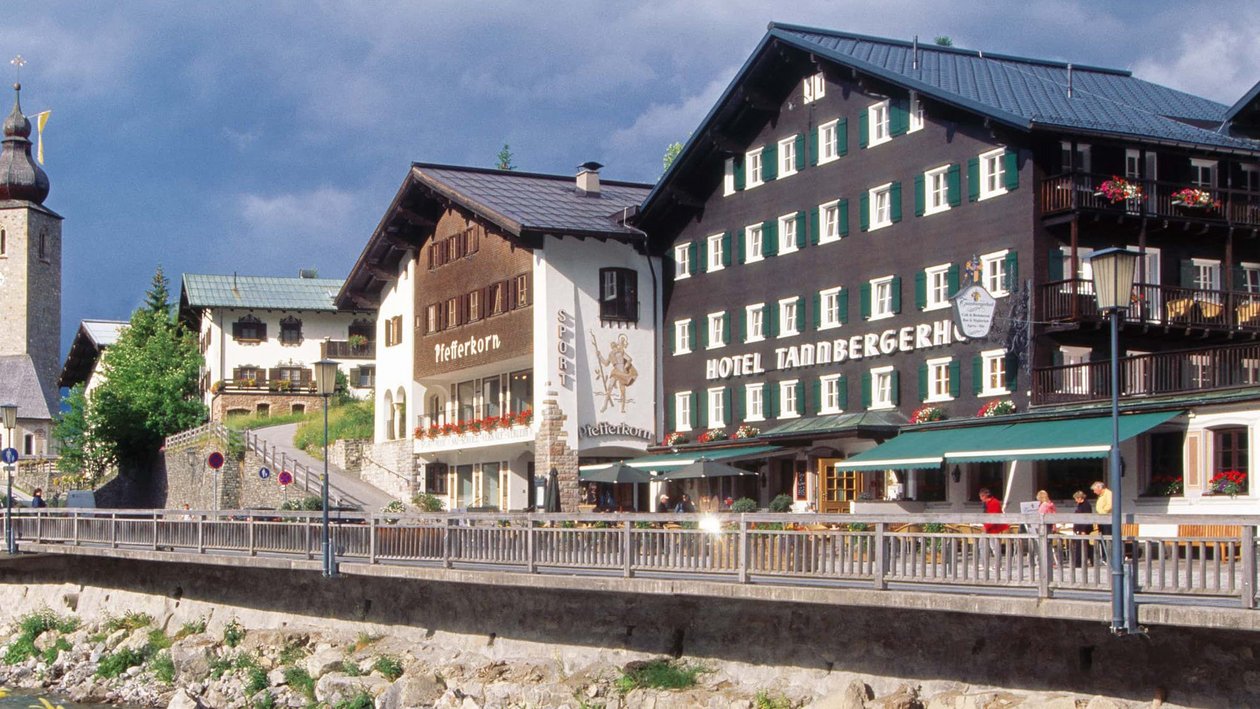 Faszinierende Bergarchitektur am Tannbergerhof Hotelgebäude mit malerischer Aussicht auf Berge und einen Fluss im Vordergrund unter bewölktem Himmel