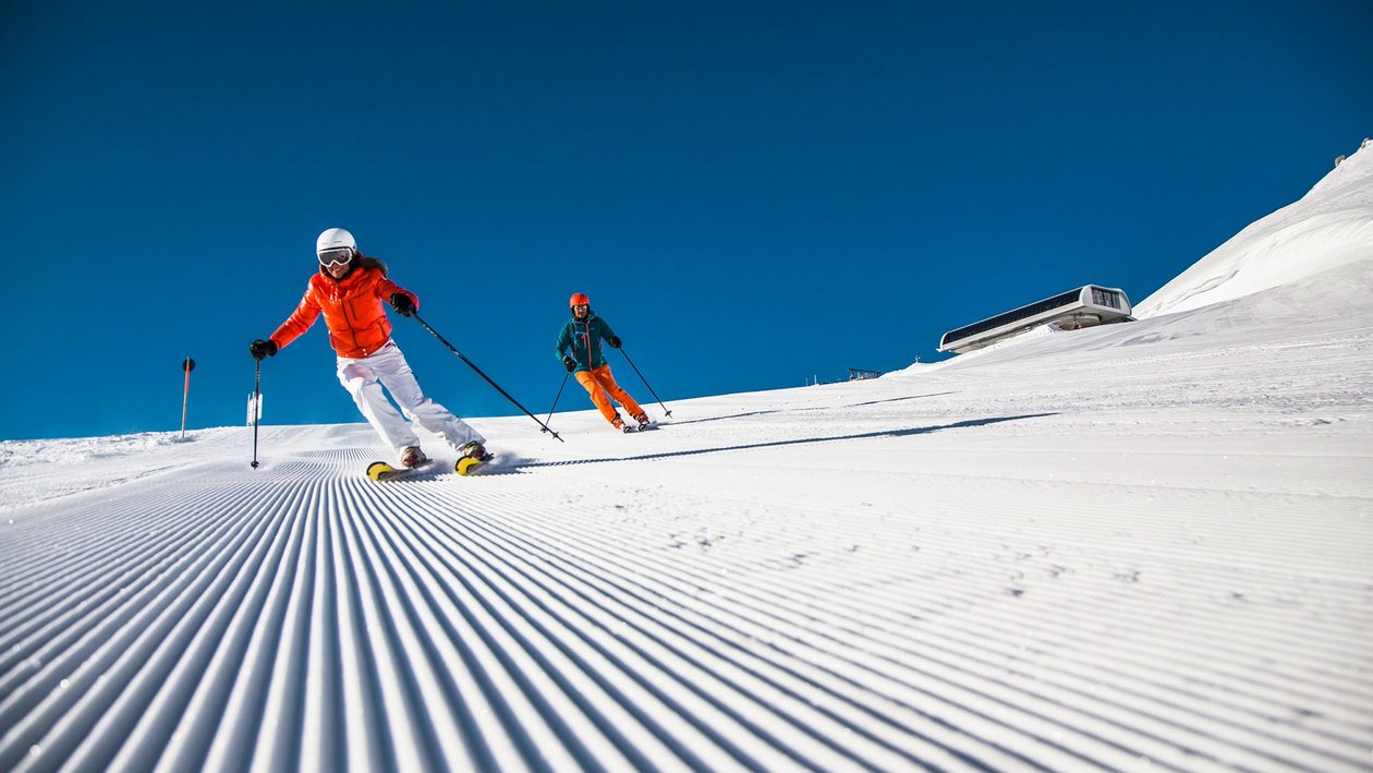 Skifahren im Arlberg Zwei Skifahrer auf einer frisch präparierten Piste unter blauem Himmel in den Bergen