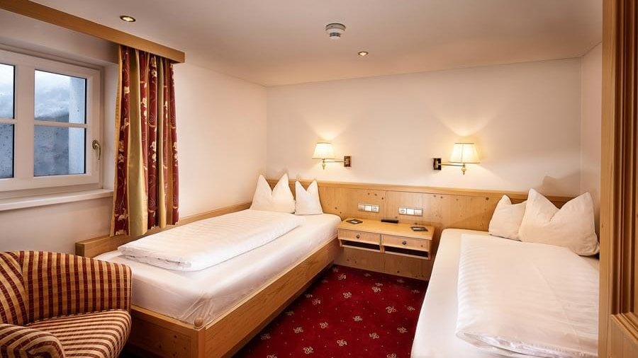 Familienzimmer mit geteilten Betten Hotelzimmer mit zwei Einzelbetten und einem gepolsterten Sessel in warmem Licht.
