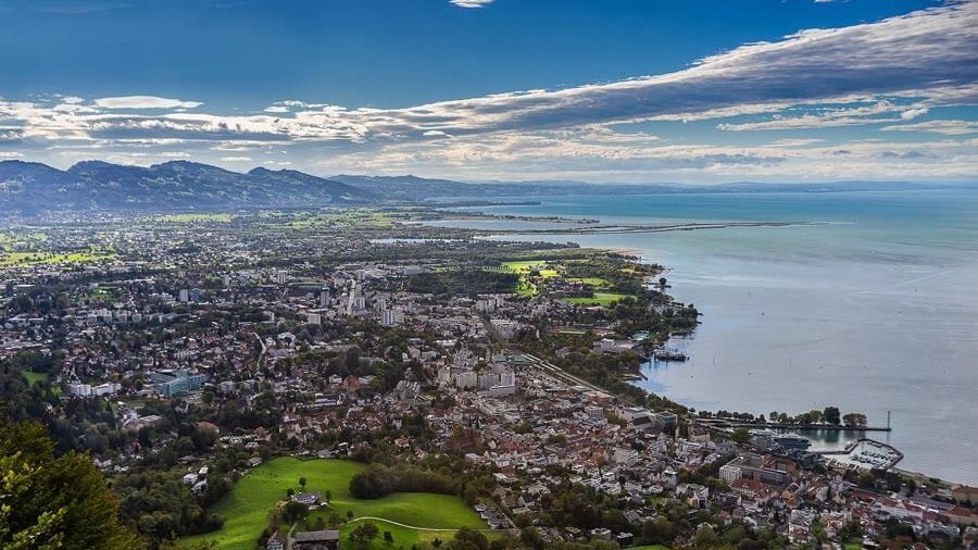 Panoramablick auf Bregenz Städtische Landschaft mit Blick auf den Bodensee und umgebende Berge unter bewölktem Himmel
