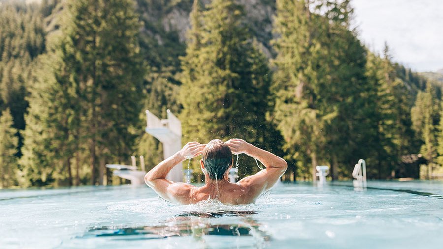Entspannung im Freiwasser Person schwimmt in einem Außenpool mit Vorarlberger Berg- und Waldkulisse im Hintergrund © Daniel Zangerl