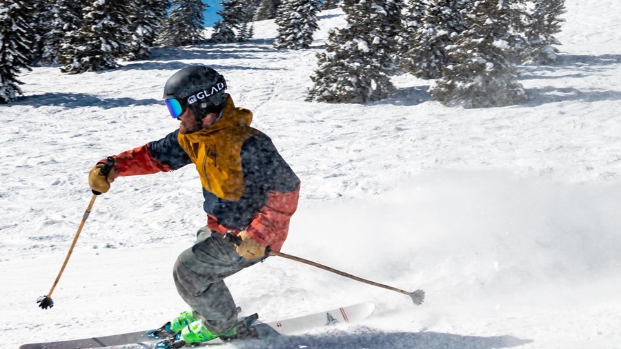 Schneeabenteuer am Arlberg Skifahrer fährt durch eine schneebedeckte Landschaft mit Bäumen im Hintergrund und aufwirbelndem Schnee