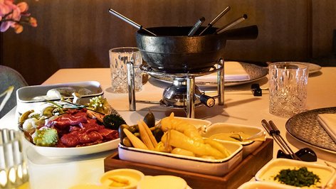 Kulinarische Vielfalt im Hot Pot Fondue-Set mit Fleisch, Gemüse, Saucen und Beilagen auf einem gedeckten Tisch im Tannbergerhof in Lech © Robert Stocker