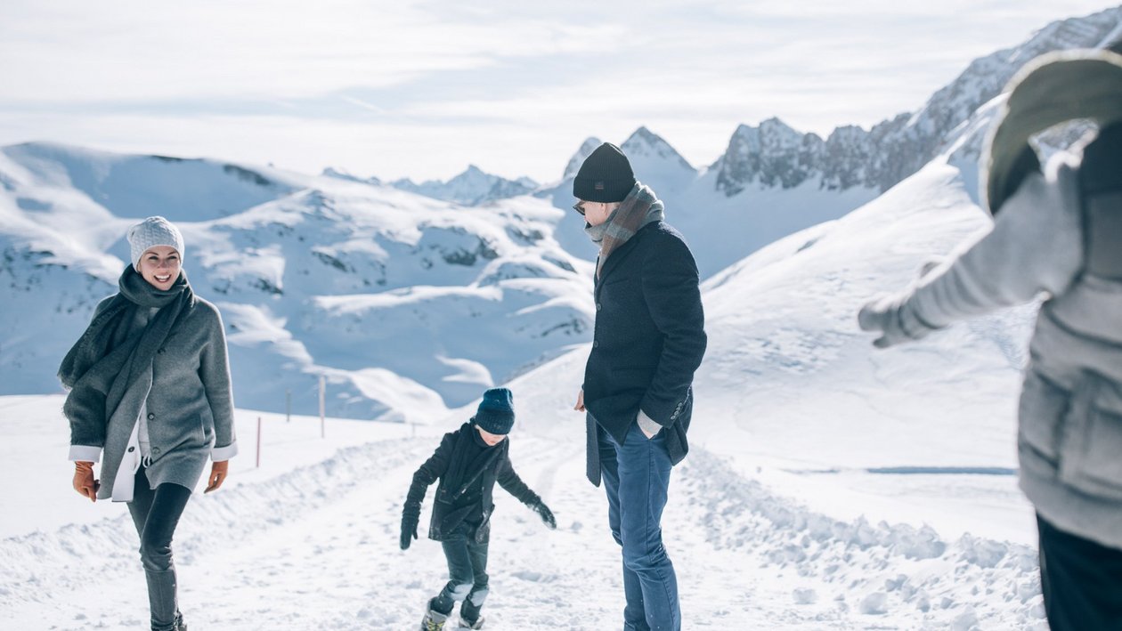 Familienwinterwanderung in den Bergen Familie wandert durch eine verschneite Landschaft mit Bergen im Hintergrund in Winterkleidung.