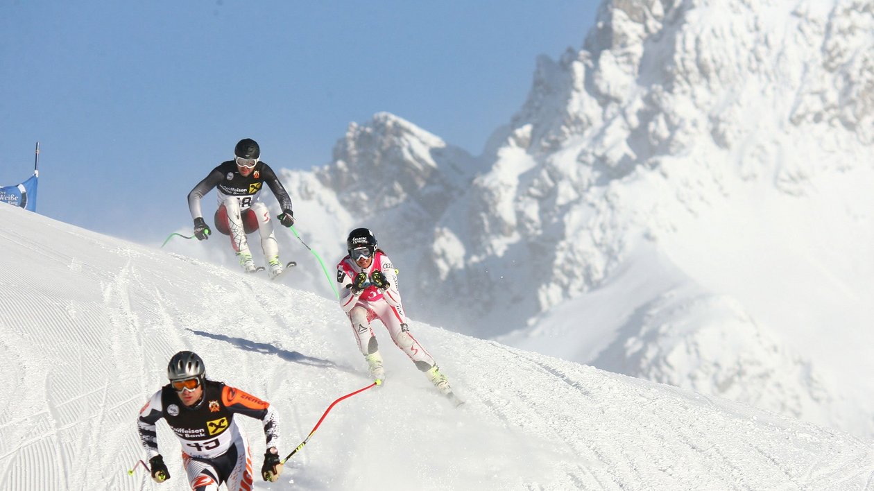 Skifahrer auf der Piste Drei Skifahrer rasen die verschneite Piste hinunter mit Berglandschaft im Hintergrund.