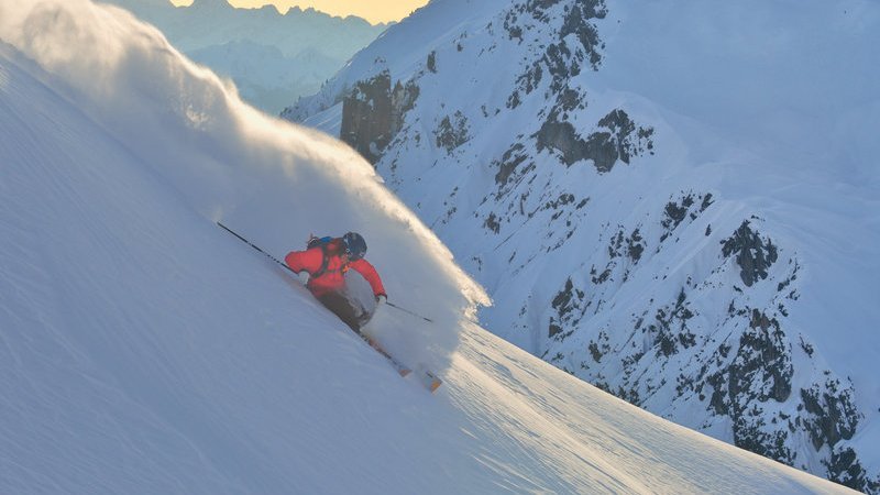 Skifahren in den Alpen Skifahrer fährt die schneebedeckte Piste hinunter, umgeben von Bergen und winterlicher Landschaft.