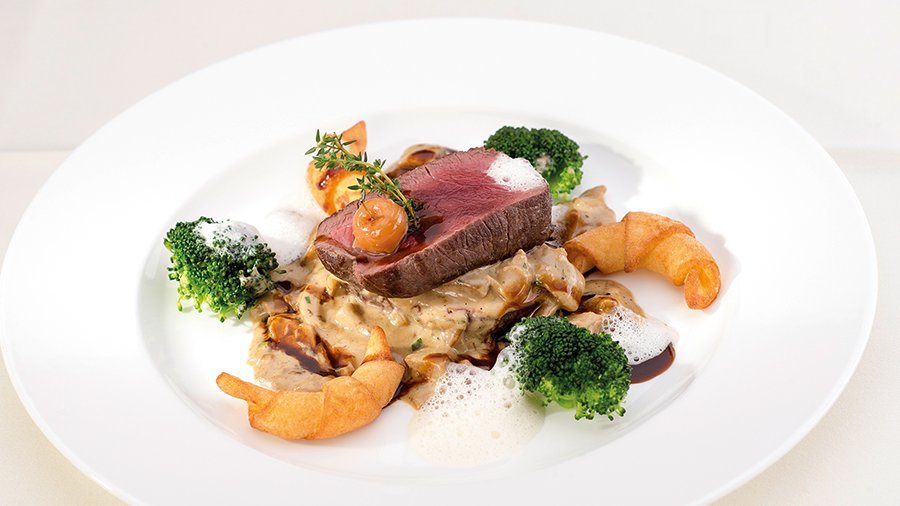 Feines Rindfleischgenuss im Tannbergerhof Ein elegantes Gourmetgericht mit zartem Rindfleisch, Brokkoli und Garnelen auf einem weißen Teller.