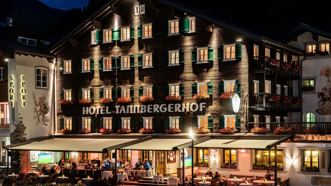 Beleuchteter Tannberger Hof bei Nacht Außenansicht des Tannberger Hof Hotels mit beleuchteten Balkonen und Terrasse in der Nacht