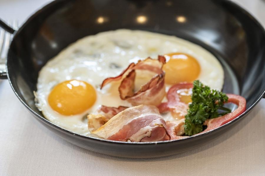 Frisches Frühstück mit Spiegeleiern Spiegeleier mit Speck und Gemüse in einer schwarzen Pfanne © Foto Lehmann