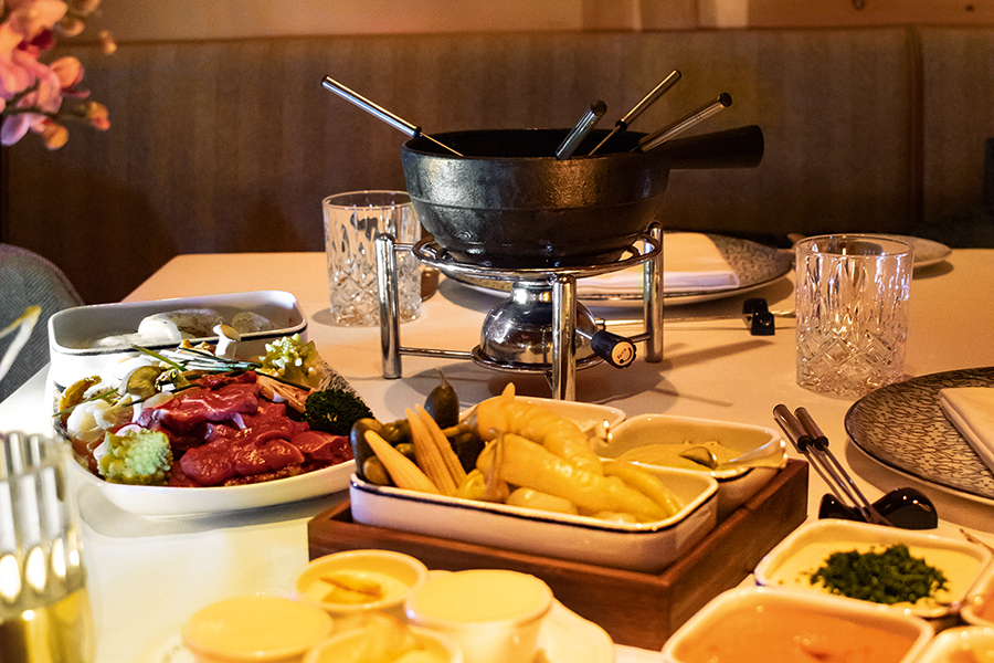 Kulinarische Vielfalt im Hot Pot Fondue-Set mit Fleisch, Gemüse, Saucen und Beilagen auf einem gedeckten Tisch im Tannbergerhof in Lech © Robert Stocker