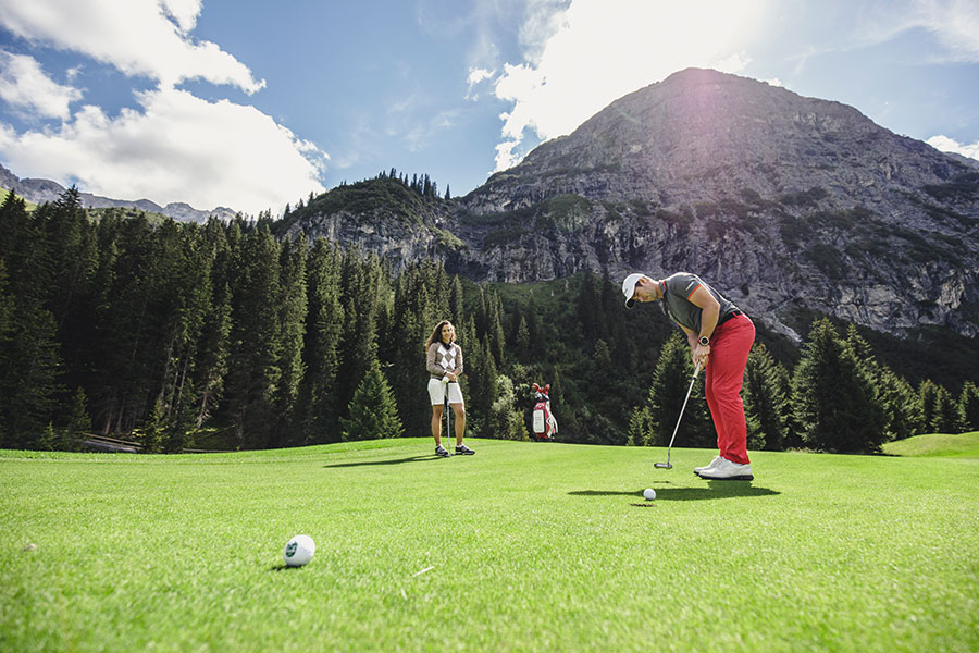 Golfvergnügen in den Alpen Golfer beim golfen mit Vorarlberger Bergkulisse und zwei Begleitpersonen im Hintergrund © Christoph Schoech
