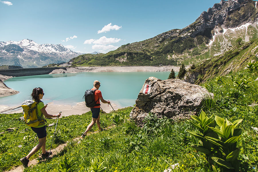 Wanderabenteuer in den Alpen Zwei Wanderer mit Rucksäcken und Wanderstöcken auf dem Min Weag mit Blick auf den türkisblauen See