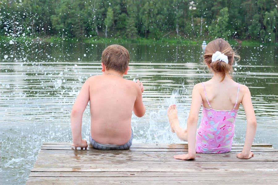 Schwimmen & Baden an heißen Sommertagen Zwei Kinder sitzen in Badekleidung an einem See auf einem Steg