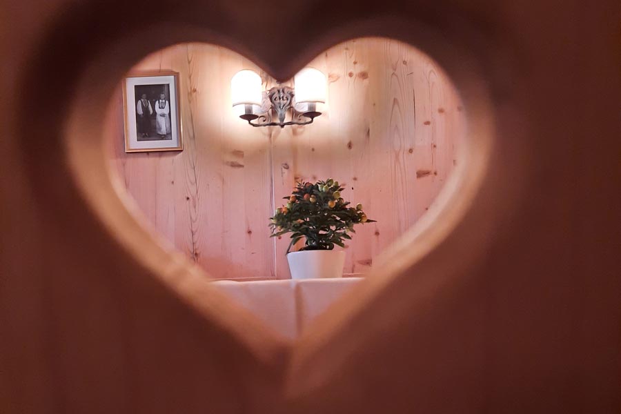 Herzförmiger Blick auf gemütliches Interieur Ein herzförmiger Ausschnitt in einer Holztür zeigt ein einladendes Innenraumdesign mit Pflanzen und Wanddekoration.