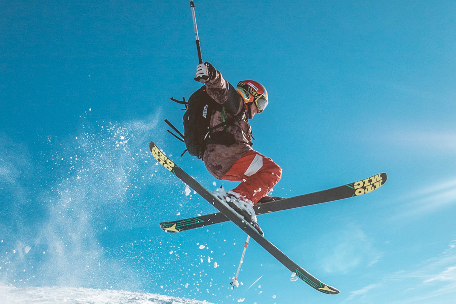 Tricks beim Freeriden zeigen Freerider springt mit gekreuzten Skiiern an einem strahlend blauen Himmel