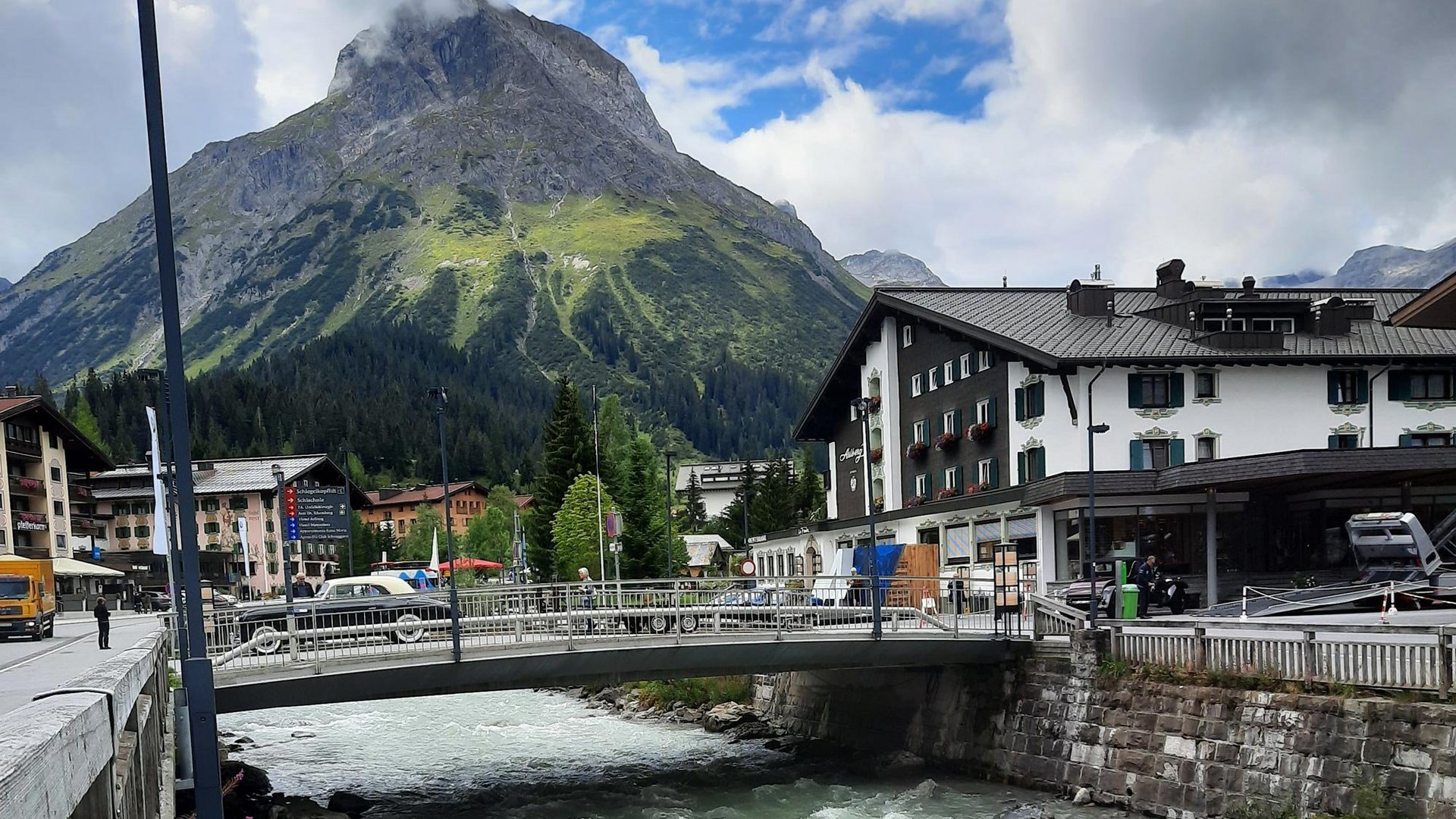 Alpine Landschaft mit Dorf und Fluss Idyllisches alpenländisches Dorf mit einem Fluss und Bergen im Hintergrund unter einem teils bewölkten Himmel