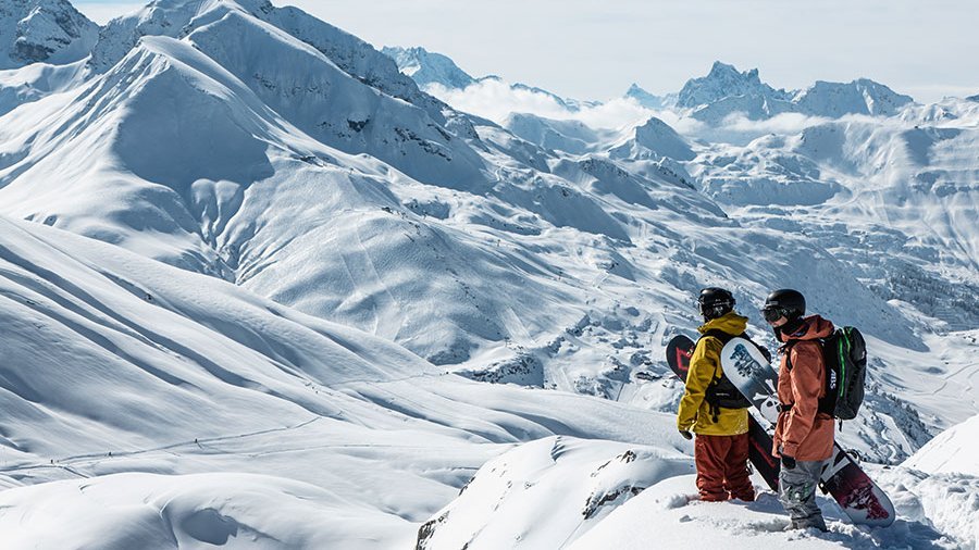 Abenteuer im Schnee erleben Zwei Snowboarder auf einem schneebedeckten Gipfel mit Blick auf die Winterlandschaft und Berge