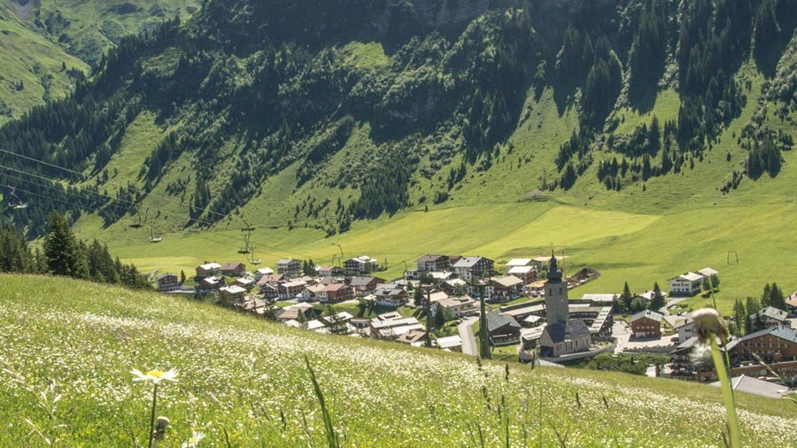 Alpines Dorf in traumhafter Kulisse Ein malerisches Bergdorf umgeben von Hügeln und blauem Himmel in der Natur des Arlbergs.