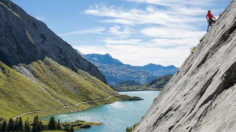 Herausforderung am Felsen Person klettert an einer steilen Felswand mit Berg- und Seelandschaft im Hintergrund
