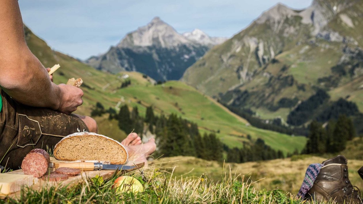 Picknick im Gebirge Person im Wanderoutfit sitzt auf Gras und genießt ein Picknick mit Brot und Salami in den Bergen