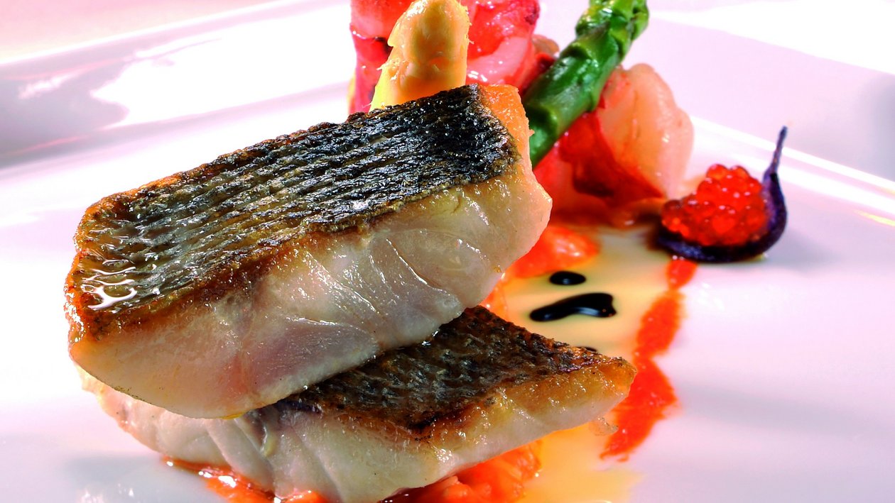 Feine Meeresfrüchte Kreation Ein Gourmet-Gericht mit Fisch und Gemüse auf einem weißen Teller präsentiert. Mit Saucen verfeinert.