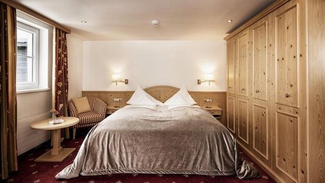 Elegantes Doppelzimmer im Tannbergerhof Furniertes Hotelzimmer mit großem Bett und Holzinterieur im sanften Licht, ideal für Erholung.